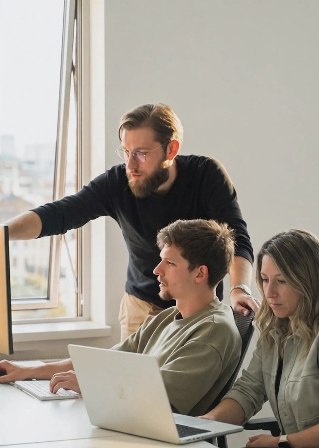 three-agency-team-members-gathered-around-a-laptop-in-a-modern-office-one-standing-and-pointing-at-the-scr