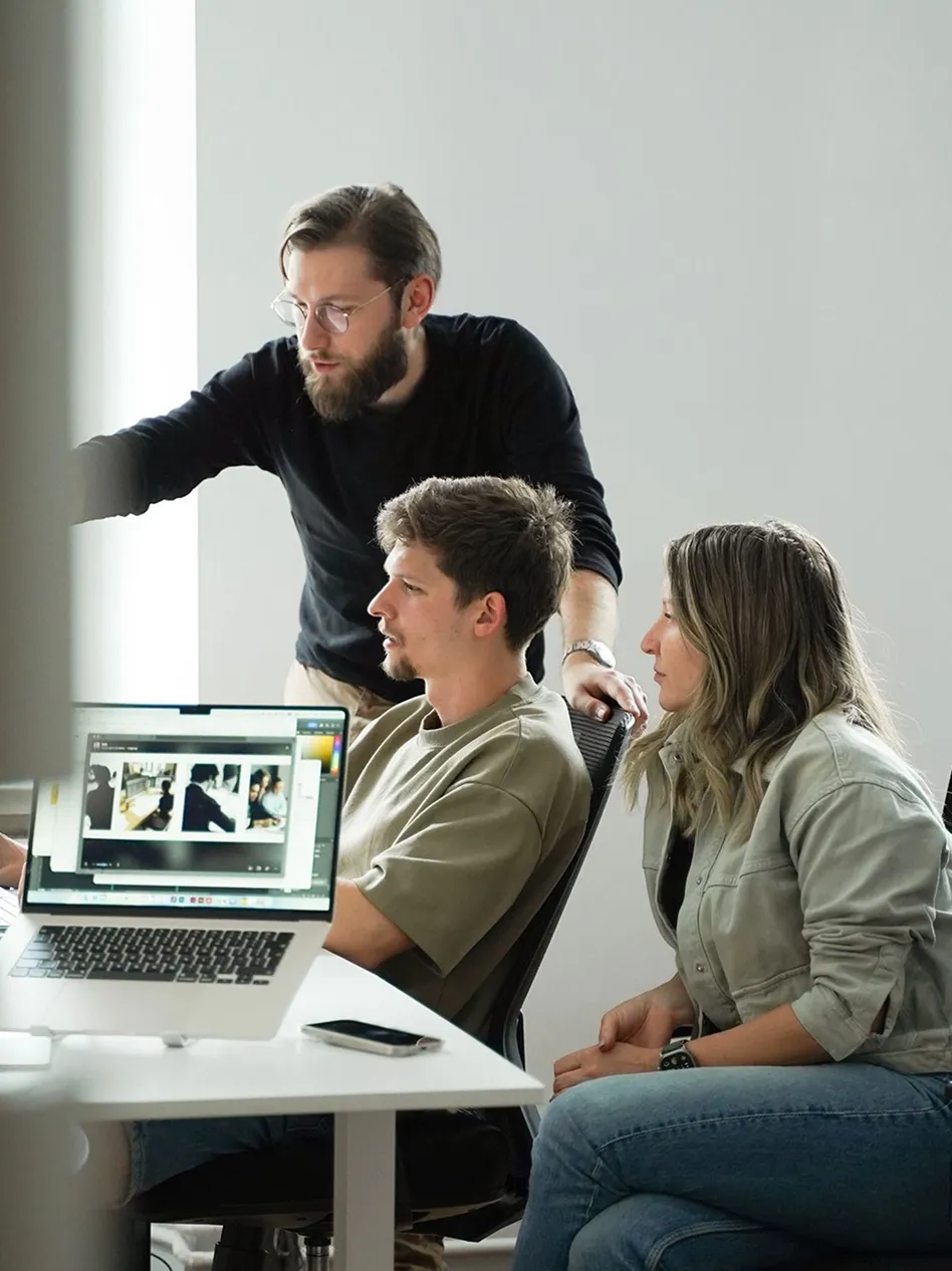 Three agency team members gathered around a laptop in a modern office — one standing and pointing at the screen — with use case cards for WordPress development, marketing agencies, digital products, and freelancers visible on the right.